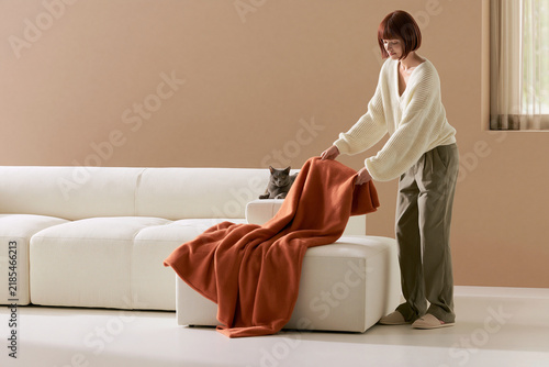 Photorealistic woman arranging a blanket beside a cat on the sofa