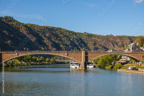 Fotografie Scenic stone arch bridge spanning a wide river with tourist boats and a forested