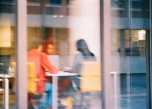 Diverse business team collaborating in conference room viewed through glass window with reflection