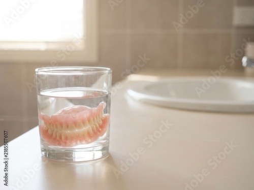 A plain generic full set of dentures resting in a clear glass of...
