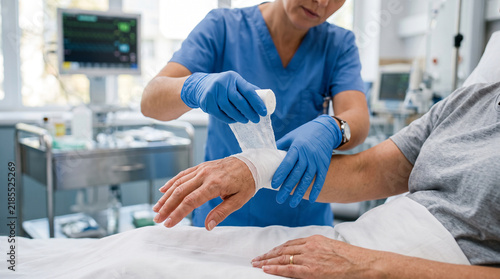 Healthcare professional applying a gauze bandage to a senior patient's wrist in a hospital setting.