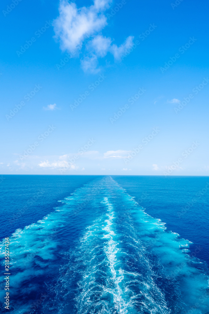Obraz premium Water wake trail left by cruise ship in deep blue ocean under clear sky with copy space