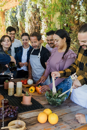 Group of Latin American Adult Students With Teacher Preparing recipe ingredients in Cookery Class in Mexico. Hispanic people multi generations learning together to cook in a terrace outdoors