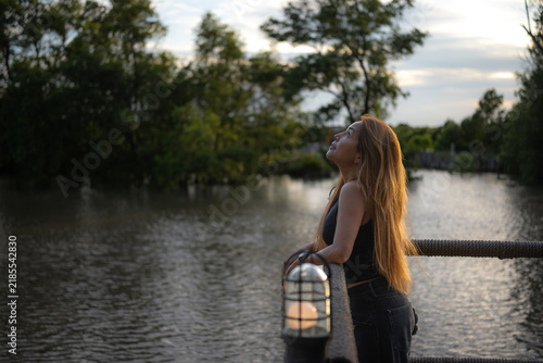 A long-haired Asian woman stands by the river in the evening.