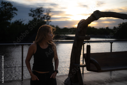 A long-haired Asian woman stands by the river in the evening.