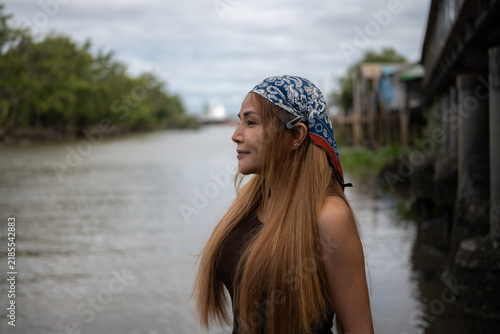 A long-haired Asian woman stands by the river in the evening.