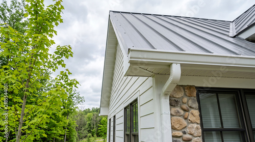White house exterior with gray metal roof, stone accents, and green trees architecture building