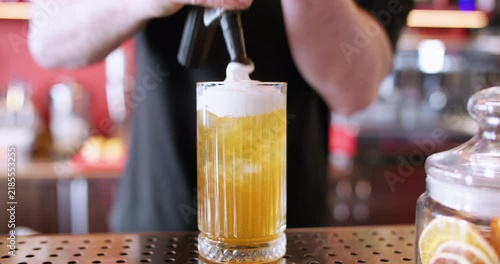 Garnishing beverage. Cream soda recipe. Barkeeper male hand adding white whipped foam top with siphon to yellow iced cocktail glass.