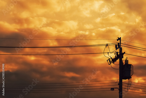 Silhouette of an electricity pole and power lines against a dramatic orange cloudy sky. Heatwave weather and energy industry concept background.