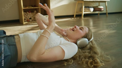 Girl lies on the floor wearing headphones while listening to music in a room with wooden furniture during the day