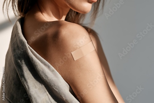Young woman with a medical adhesive plaster band-aid on her upper arm after vaccination, close-up shoulder view.