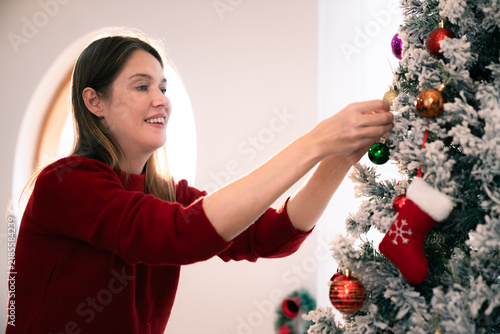 Caucasian woman decorating Christmas tree with ornaments at home