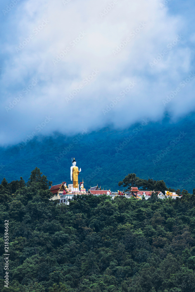 Obraz premium Standing Buddha Statue at Wat Phra That Doi Kham Temple, Chiang Mai, with Misty Mountain Landscape