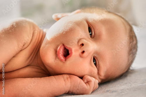 Foto An awake newborn baby lies on pale bedding with an open mouth and a tiny hand beside the cheek