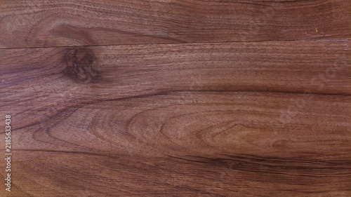 a close-up view of a polished wooden surface with a rich, reddish brown hue. The natural grain of the wood runs horizontally across the frame