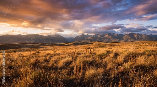 Golden Grassland Prairie Extending Toward Mountain Range Under Dramatic Sunset Sky
