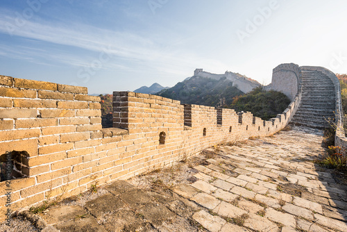 Bild auf Leinwand A section of ancient stone and brick Great Wall winding along mountain ridges under a clear blue sky, showing historic defensive architecture