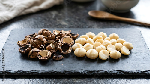 Shelled macadamia nuts resting beside their cracked husks on a textured slate board