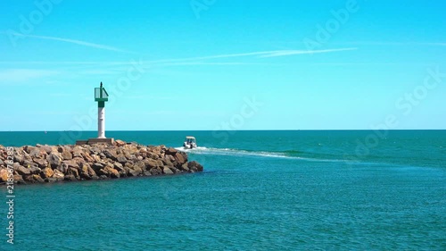 Boat sails past green light on rocky jetty. Valras, France .
