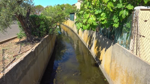 Water flows slowly in the channel beside a path. Valras, France .