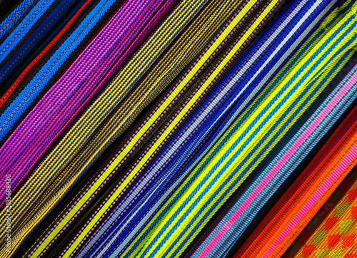 Close-up of colorful, woven fabric straps, nylon webbing, or elastic bands arranged in parallel diagonal lines. Various colorful, textured woven straps