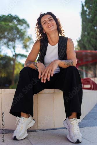 A beautiful young woman with curly hair, smiling on a sunny day. Curly hair. A confident woman in the city.