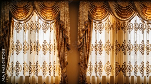 Rich gold and ivory drapes frame sheer curtains with ornate embroidery. These luxurious window coverings add elegance to any opulent interior decor setting.