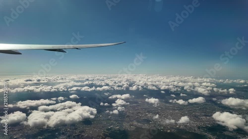 An airplane wing flies high above clouds and land.