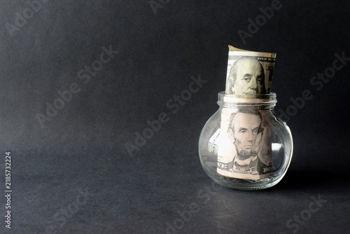 Fotografie US dollar bill with Benjamin Franklin portrait inside a clear glass jar on a black background
