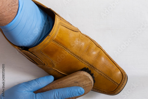 Polishing brown leather slip on shoe with a shoe polishing brush. On a white wood background.