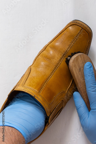 Polishing brown leather slip on shoe with a shoe polishing brush. On a white wood background.