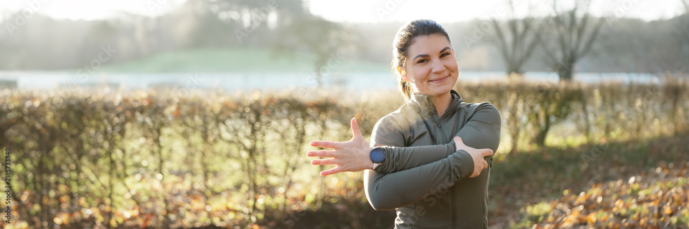 Fototapeta premium Athletic young woman is stretching after workout, training and running on a beautiful winter morning, panoramic view 