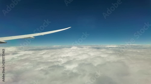 An airplane wing flies above a sea of white clouds.