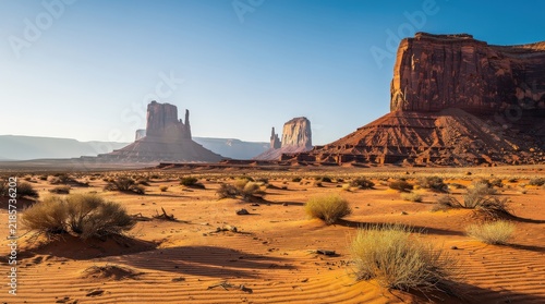 Vast desert landscape with iconic red rock formations under a clear blue sky, showcasing the rugged beauty of Monument Valley.