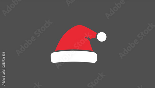 Christmas santa claus red hat with a white fluffy trim and pompom centered on a solid dark grey background.