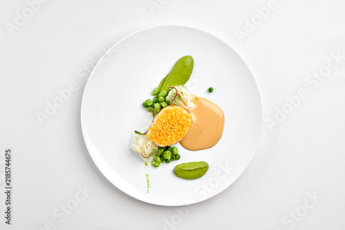 Top view of a gourmet fish fillet dish with green pea puree, creamy sauce, and edamame on a white plate, isolated on white background.