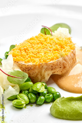 Macro detail of a crust-topped fish fillet served with green pea puree, edamame, and sauce on a white plate.