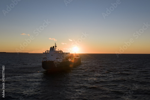Aerial drone view of a large cargo ship navigating the choppy waters of the Baltic Sea during a dramatic golden sunset near the coast.