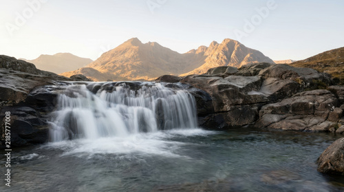 Silky smooth waterfall with sunlit mountain scenery creates tranquil wilderness view and invites peaceful reflection beside clear water