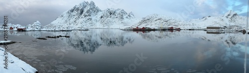 Panoramic winter view of a fjord with coastal cabins and snow-covered mountains, Lofoten Islands, Norway