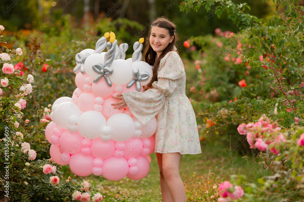 Fototapeta premium A girl in a rose garden, wearing a romantic dress, is holding a marshmallow cake and blowing out the birthday candles.