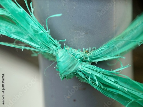 Quadro su tela Macro Detail of a Turquoise Green Plastic Raffia Rope Knot Tied to a Grey Pipe