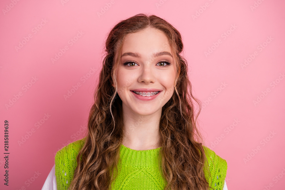 Obraz premium Young smiling female student with braces wearing a bright green vest style sweater against pink background showcasing happiness school fashion lifestyle and casual youth vibe