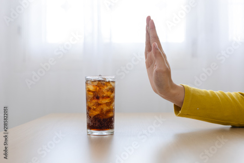 Foto Sugar reduction concept, person refusing glass of sugary soda with ice on table at home, healthy choice, nutrition, wellness, diet, prevention, lifestyle