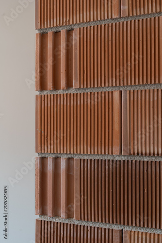 Textured terracotta brick wall with alternating smooth and ridged courses, vertical grooves, mortar joints, warm earthy tones, and repeating architectural pattern