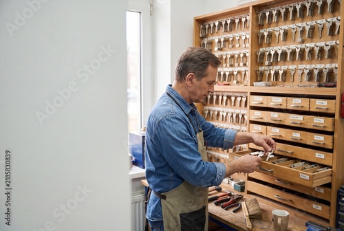 Locksmith Choosing Replacement Key From Organized Storage Drawer in Workshop