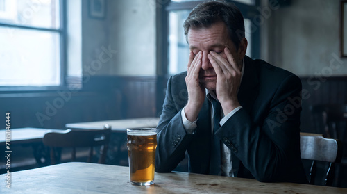 Depressed lonely man sitting at bar counter holding head in despair