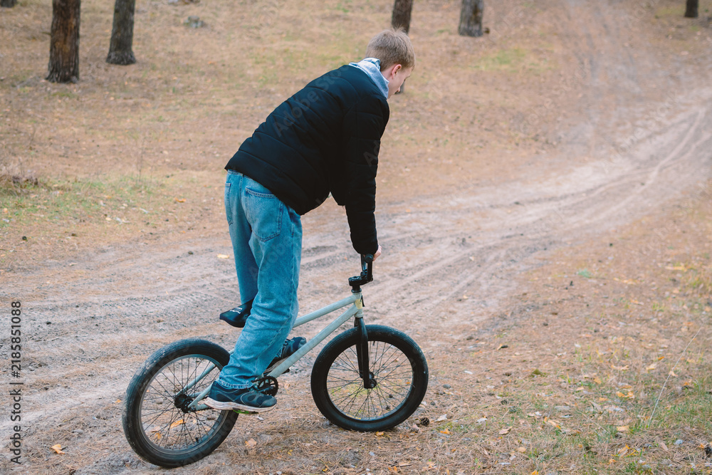 Obraz premium Young man riding a bmx bike on a dirt path in a pine forest during autumn outdoor activity