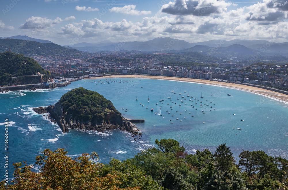 Obraz premium Vista panorámica elevada de la bahía de La Concha en San Sebastián, destacando la Isla de Santa Clara, los barcos fondeados y las montañas al fondo.