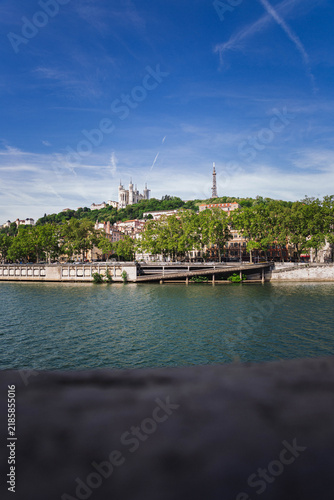 Panoramic view of Lyon, France, along the Saône River with the historic cityscape and Fourvière hill under a blue sky.